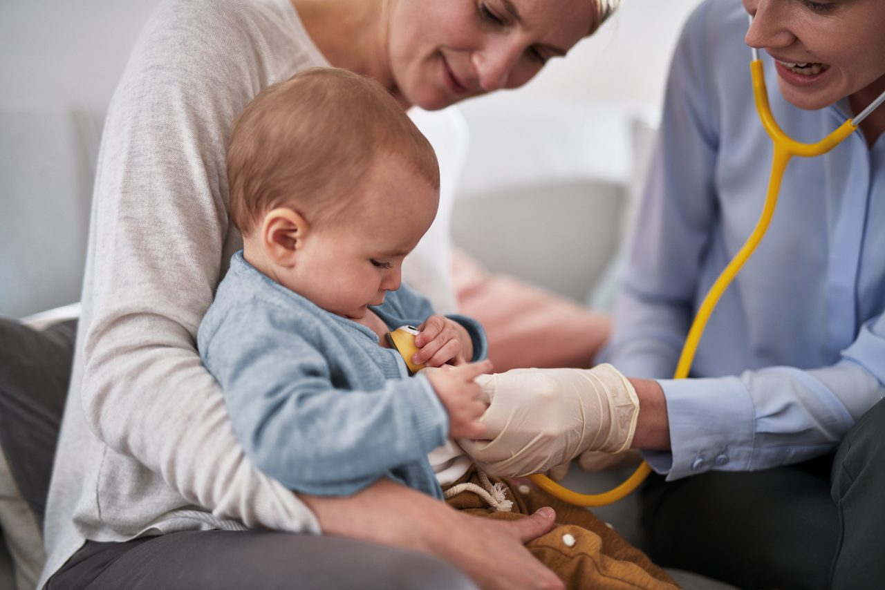 Mutter mit Baby beim Arzt. Die Ärztin hört das Baby mit einem Stethoskop ab.