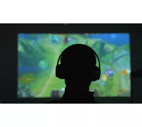 Silhouette di spalle di un uomo con delle cuffie che gioca con un videogame davanti a un grande schermo in una stanza scura