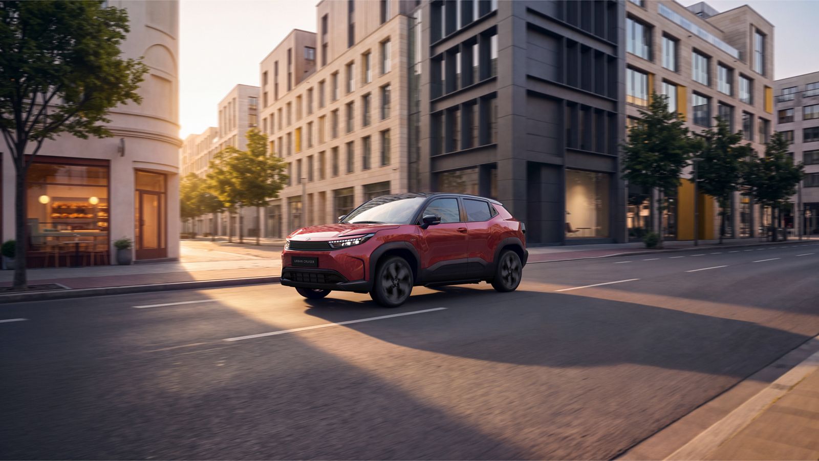Roter Toyota Urban Cruiser fährt auf einer städtischen Straße mit modernen Gebäuden im Hintergrund
